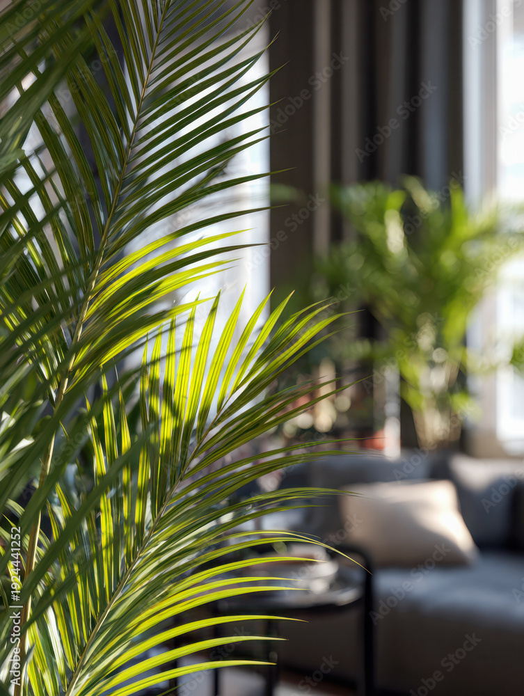 Fototapeta premium Vibrant green palm leaves illuminated by natural sunlight inside a modern living room featuring a cozy sofa and indoor plants for a refreshing ambiance