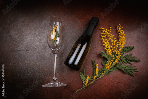 Glass with mimosa and champagne bottle on dark brown textured background