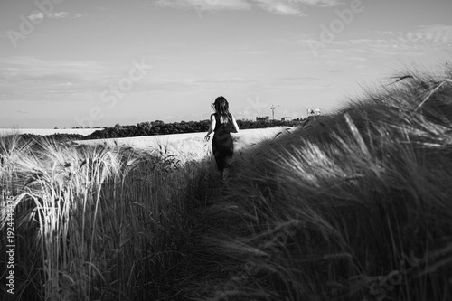 Dramatic black and white shot of a woman in a dark dress running through a tall grain field towards the horizon, symbolizing freedom, solitude, and artistic mystery