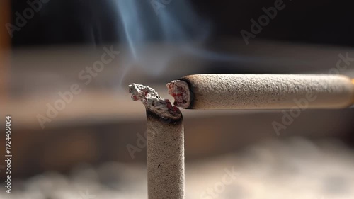 Close up of burning cigarette emitting smoke with glowing embers and ash in daylight