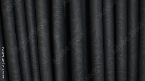 Close up of dark black curtain fabric with elegant floral pattern and vertical folds. Dramatic drapery texture background ideal for luxury backdrop, stage concept, interior design, and graphic design 