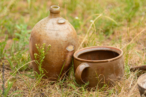 Rustic antique clay bottle and ceramic pot sitting in dry grass, outdoor rural still life