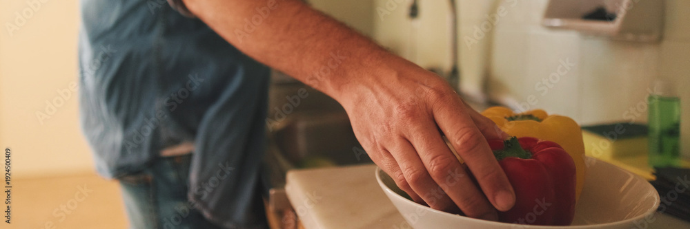 Obraz premium Close-up of the hands of guy dressed in denim shirt washing vegetables in the kitchen in the apartment, vegetables in the foreground. Panoramic