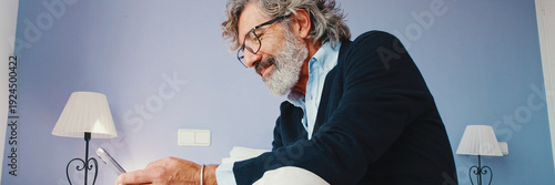 Wallpaper Mural Stylish good looking mature man is sitting on bed and using smartphone. Panoramic Torontodigital.ca
