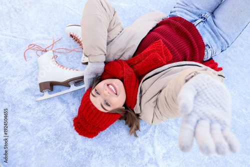 Happy young woman with ice skates lying on rink, top view