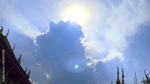 The Sun's Shining Behind Big Cloud and Parts of Roofs of Temple on Blue Sky Background with Bird Flying Compound of a Monastery at Bangkok, Thailand. 19 MAY 2025, A.M./ Slow Down Video