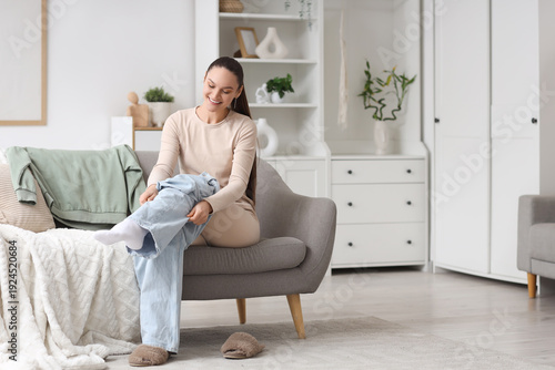 Young woman in thermal underwear putting on jeans at home