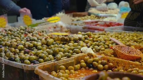 Close-up of assorted marinated green olives displayed in plastic containers at a traditional food market in Malaga, Spain. Mediterranean street food with seasoned olives, herbs and oil