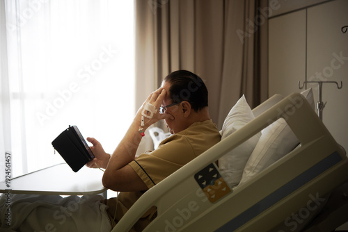Φωτογραφία Elderly man with IV line sitting in hospital bed holding tablet, contemplative e