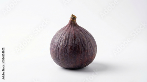 A single, ripe fig sits on a plain white surface, showcasing its unique texture and color.
