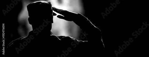 Male soldier saluting in silhouette against dark background, black and white photo  