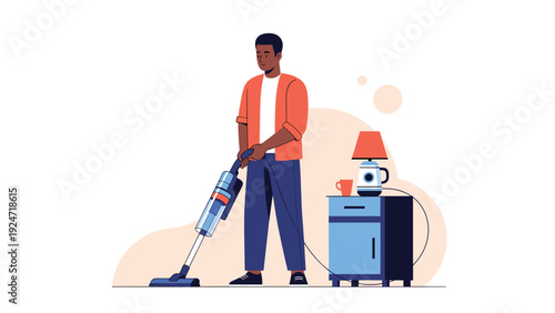 Young man using a modern handheld vacuum cleaner to clean the floor of his room near a small nightstand with a lamp.