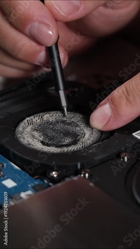 Removing dust from laptop cooling fan using screwdriver during computer repair and technical service close up of internal hardware maintenance