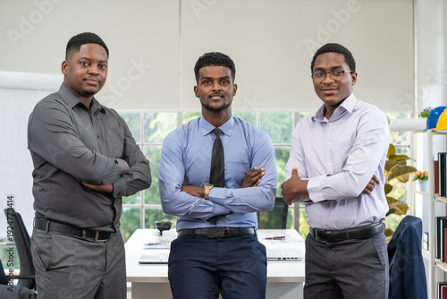 Three businessmen stood with their arms crossed in front of a desk.