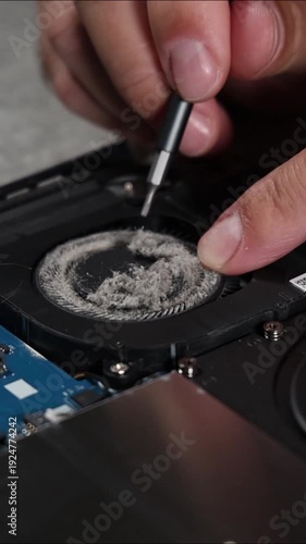 Careful cleaning of laptop cooling fan with screwdriver during internal computer maintenance and repair process close up view of dusty component to prevent overheating and improve performance