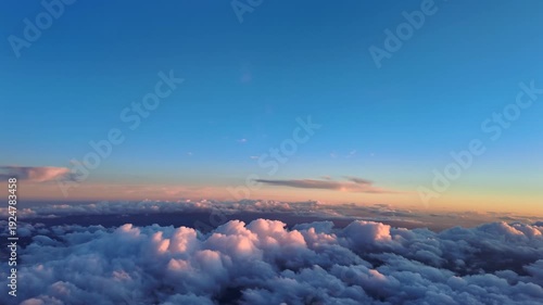 Pilot’s eye view while flying over some cottony clouds illuminated by the soft sunset light. Scene captured from a jet airplane cockpit.