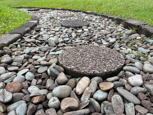 Low angle view of pebble walkway with round stepping stones, bordered by grass, ideal for garden landscaping and zen design.