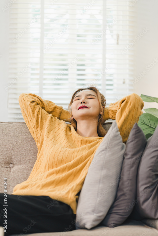 Fototapeta premium Calm young asian woman relaxing on comfortable sofa in living room enjoying peaceful lifestyle stretching arms with happy smile