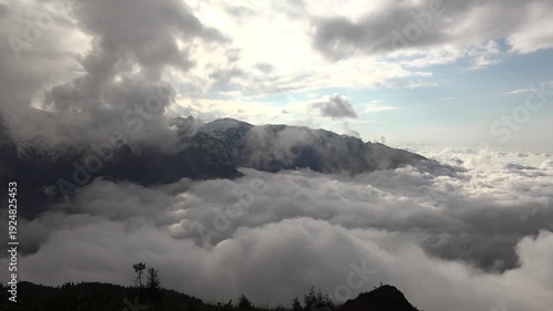 Alps mountain peaks rise above cloud sea as sunrays pierce mist, cinematic landscape view. Swiss range summits overlook overcast layer, god rays through vapor, breathtaking highland vista.