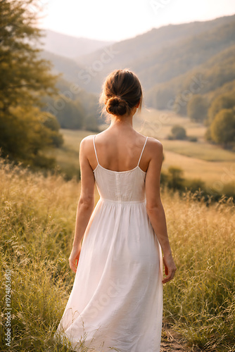 A woman in a flowing dress enjoys the picturesque landscape of a mountain valley, with a peaceful mood and sun's rays