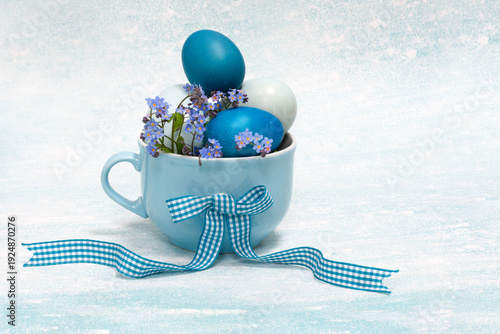 Blue color Easter eggs in light blue color cup with ribbon and decorated with forget-me-not natural blossoms, blue colored Easter composition on light blue background, Easter holiday table decoration
