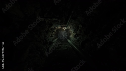 narrow utility corridor lined with service pipes and sensors, dim glow highlights wet rock and metal seams, maintenance access route suggests night shift