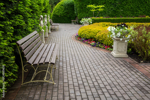 Bench for relaxing in a landscape park on a paved alley among beautiful plants. A place of relaxation in a big city.