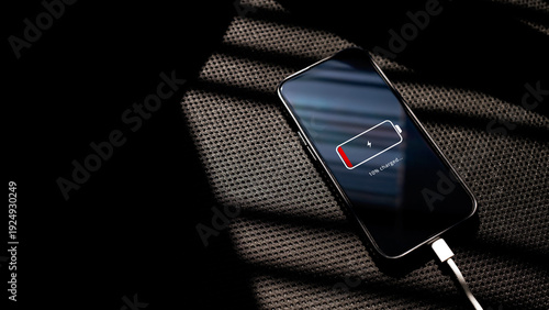 Fotografie Smartphone with low battery 10% charging via cable on a black chair textured surface