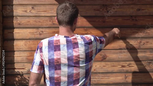 A man paints a wooden house with a brush. A man covers the wall of a wooden house with protective oil.