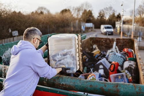 Man throwing hard plastic into recycling facility container.