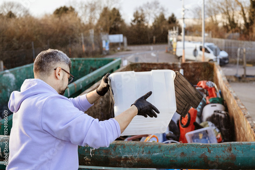 Man lowering plastic storage bin into recycling container.