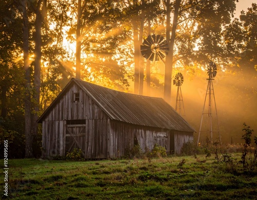 Rustic wooden barn bathed in golden sunlight with windmills in the background, a serene rural scene.