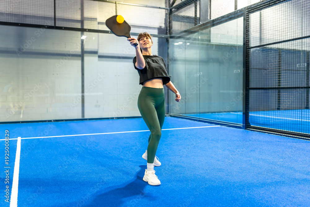 Fototapeta premium Woman playing pickleball, hitting ball during game
