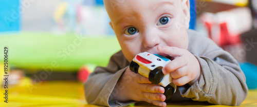 Obraz na plátně A joyful baby is lying on a vibrant play mat, happily exploring a small toy car