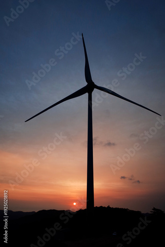 The sun is rising behind the wind turbines.