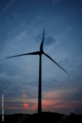 The sun is rising behind the wind turbines.