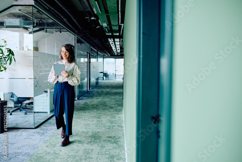 Obraz na plátně Businesswoman walking through a contemporary office corridor, smiling and engros