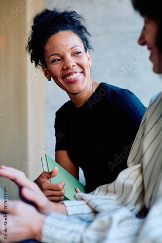 Bild auf Leinwand Happy black woman holding a notebook and smiling while listening to a colleague