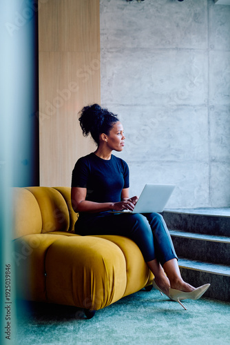 Canvas Print Focused professional woman working on a laptop while sitting on a comfortable ye