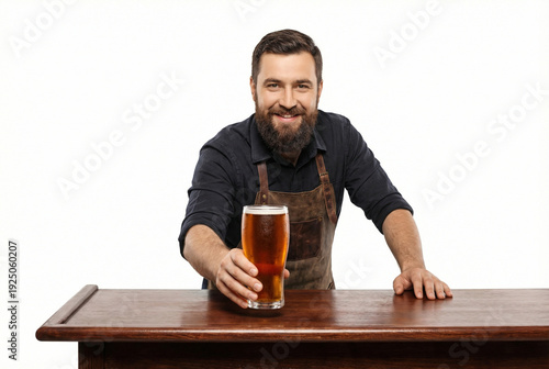 Smiling bearded bartender in apron serving fresh craft beer in a glass at the wooden bar counter isolated on white background.