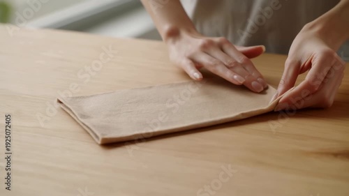 Closeup Of Hands Delicately Organizing Reusable Cloth On Wooden Surface In Peaceful Kitchen Setting