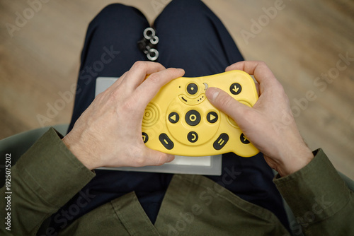 Blind man using tactile braille electronic device with large yellow buttons while sitting in library, hands holding assistive technology for visually impaired