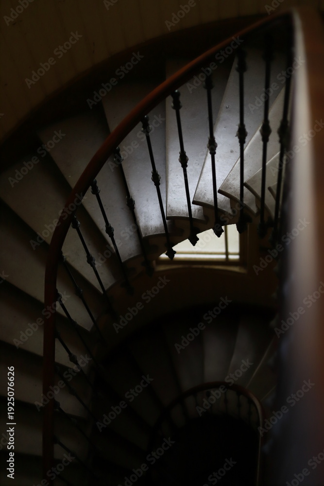 Fototapeta premium Top down view of a vintage wooden spiral staircase with a window. High-angle shot of a classic wooden spiral staircase in an old house. The composition features elegant curves, wrought iron railings, 