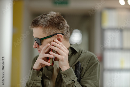 Slika na platnu Caucasian young adult man wearing sunglasses holding smartphone near ear sitting