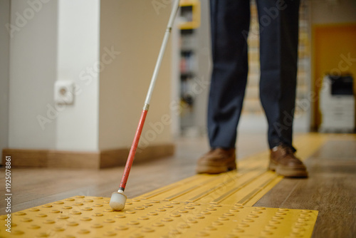 Fotografie Man using cane for navigation inside library, following tactile paving with feet