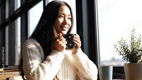 Smiling young woman enjoying warm drink by sunny window, embracing a peaceful and cozy moment indoors