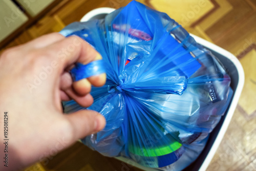 Hand holding blue garbage bag with household waste. Taking out trash from apartment. Daily routine and home cleaning concept.
