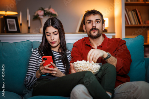 Valokuva Man watching football on TV while woman scrolling using smart phone