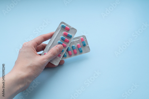 Foto Woman holding blister pack with pink and blue antibiotic capsules on light blue background