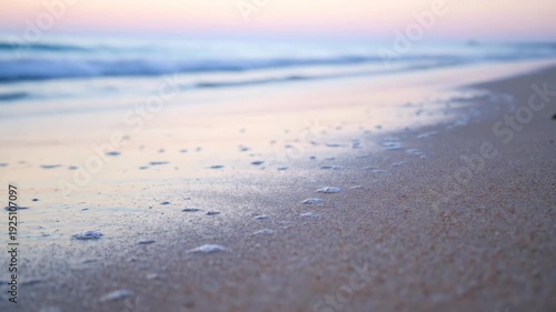 Close-up of beach at sunset. Foamy water on wet sand, blurred waves